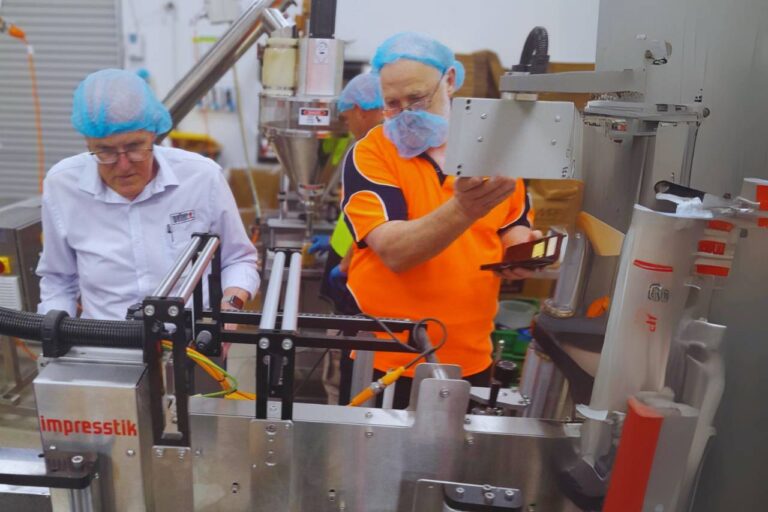 two workers in front of a labelling machine.