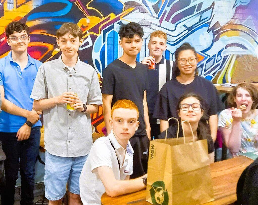 Eight young people standing and sitting in front of a bright mural.